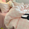 A pink plaid duvet cover set with matching pillowcases and a fluffy stuffed animal on a bed.