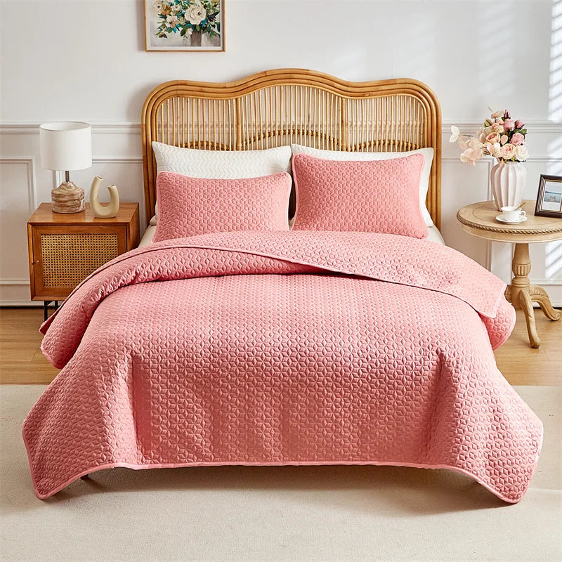 A pink quilted duvet and pillow set displayed on a bed with a light wood headboard.