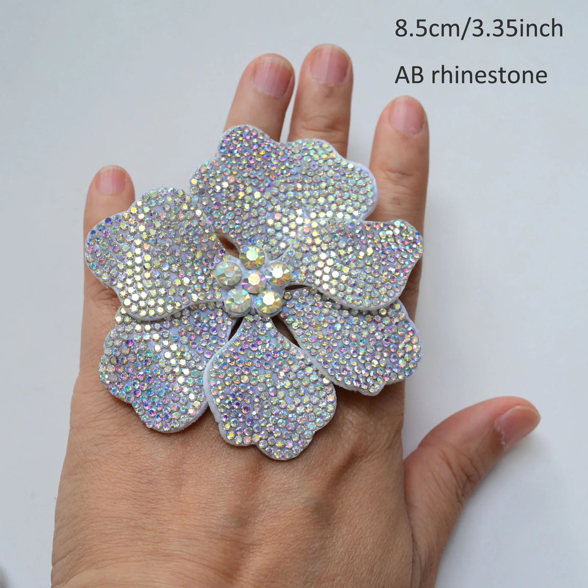 Silver rhinestone flower applique patch being held on a person's hand.