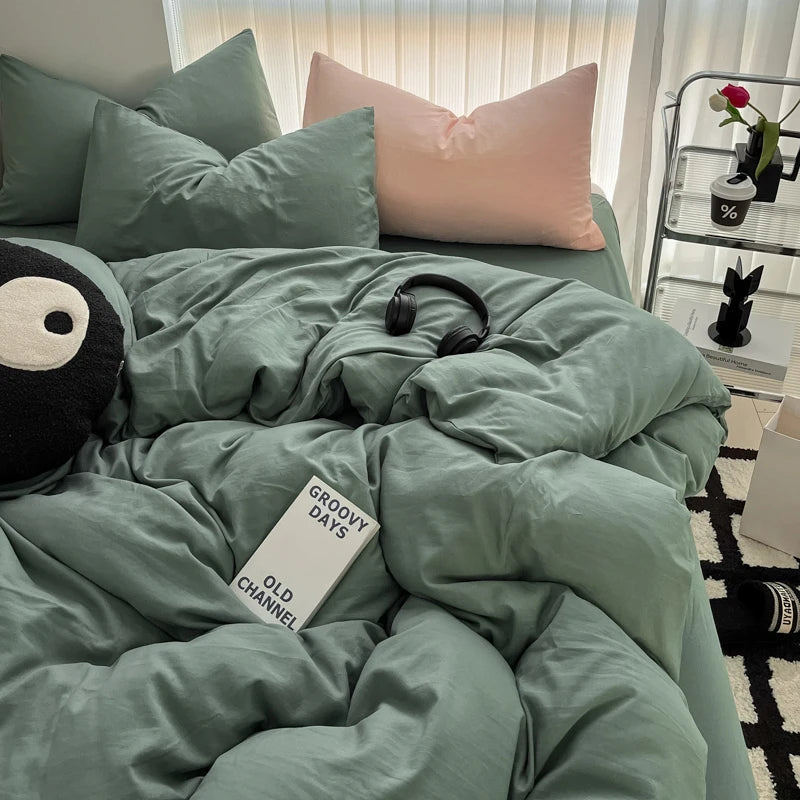 A close-up of a sage green duvet cover and pillows on a bed, featuring a black headphone and a white sign.