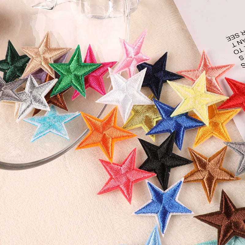 A collection of 20 five-pointed star embroidery patches in various colors and shades laid out on a light surface.