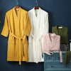 A yellow cotton terry robe hanging next to a white one against a dark blue wall.