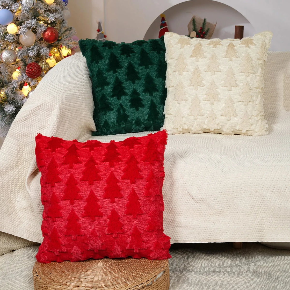Three decorative knitted Christmas cushion covers in red green and cream resting on a light-colored sofa.