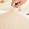 A hand is adjusting the fabric of a beige stretchable chenille sofa cushion cover.