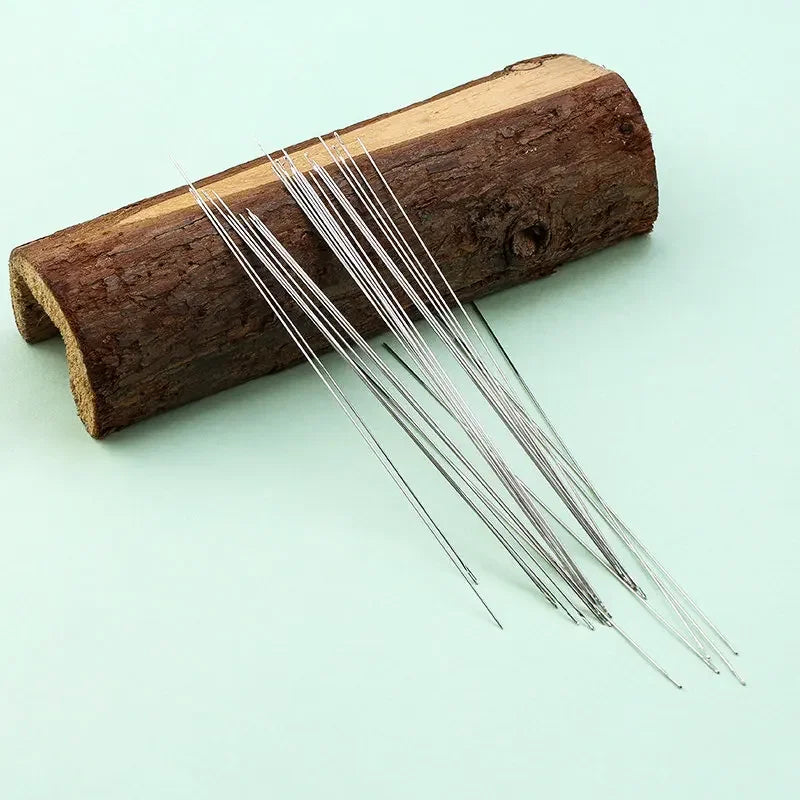 A set of precision stainless steel beading needles resting on a piece of dark wood.