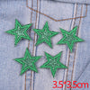 Five green glitter star patches embroidered on a denim fabric with orange stitching.