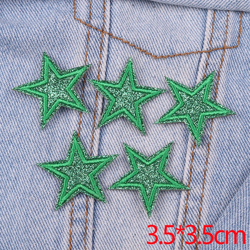 Five green glitter star patches embroidered on a denim fabric with orange stitching.
