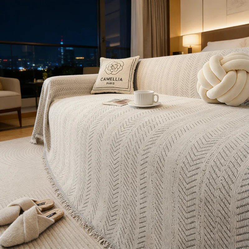 A bed featuring a beige textured duvet, decorative pillows, and a white cup on the bed.