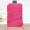 Pink crochet yarn in a skein with a dark green bobbin resting on a woven mat.