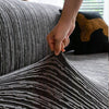 A hand is adjusting a dark gray and black striped jacquard plush elastic sofa cover on a sofa.