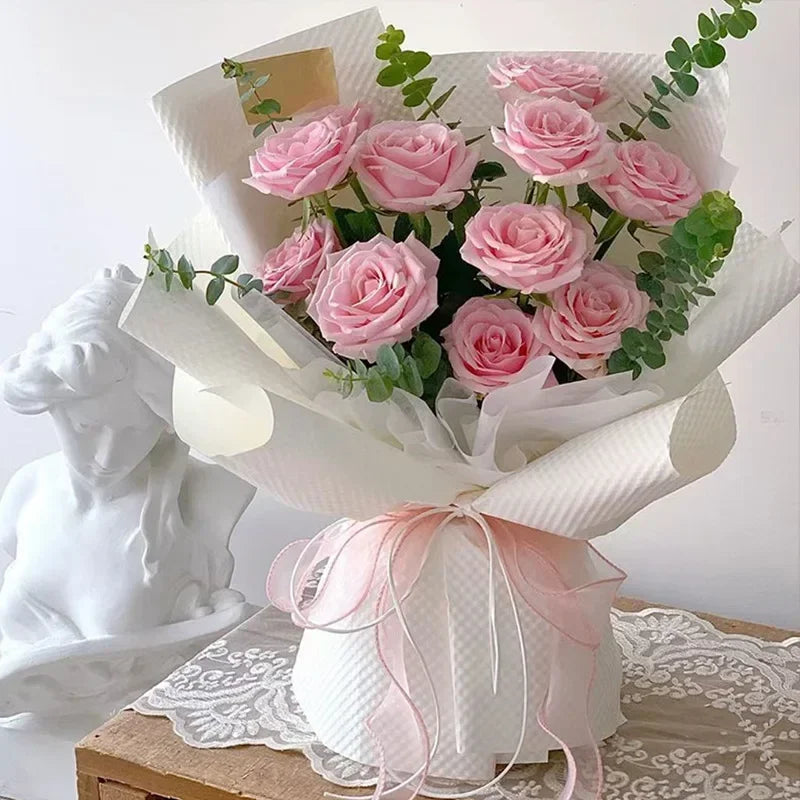 A bouquet of pink roses wrapped in white paper and tied with a pink organza ribbon.