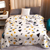 A white fleece blanket with black and yellow geometric patterns is displayed on a bed.