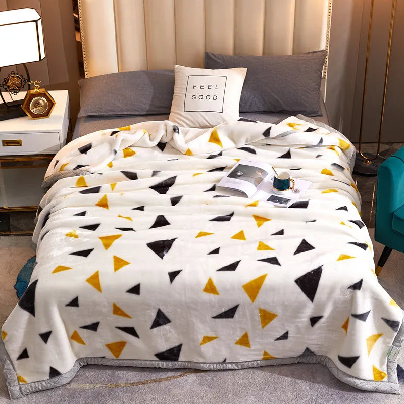 A white fleece blanket with black and yellow geometric patterns is displayed on a bed.
