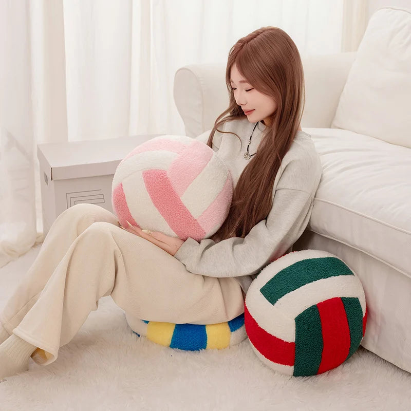 A woman is sitting on a white sofa holding a pink and white plush volleyball ball cushion.