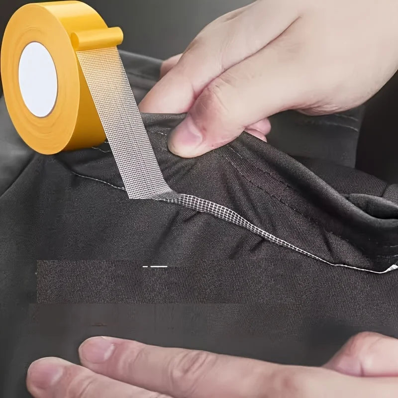 A hand is applying a roll of yellow no-sew hem tape to a dark fabric for quick folds or repairs.
