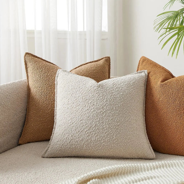 A close-up of a light beige textured boucle throw pillow resting on a neutral sofa with brown accent pillows.