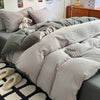 A close-up of a light gray quilt bedding set featuring a textured fabric and a small stuffed animal on a bed.