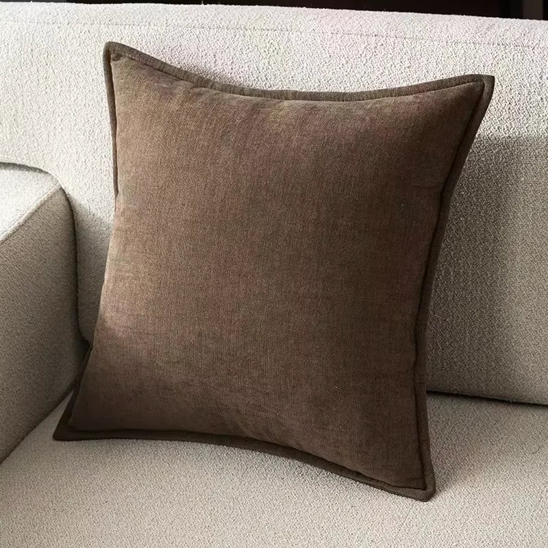 A square, dark brown chenille throw pillow resting on a light beige sofa cushion.