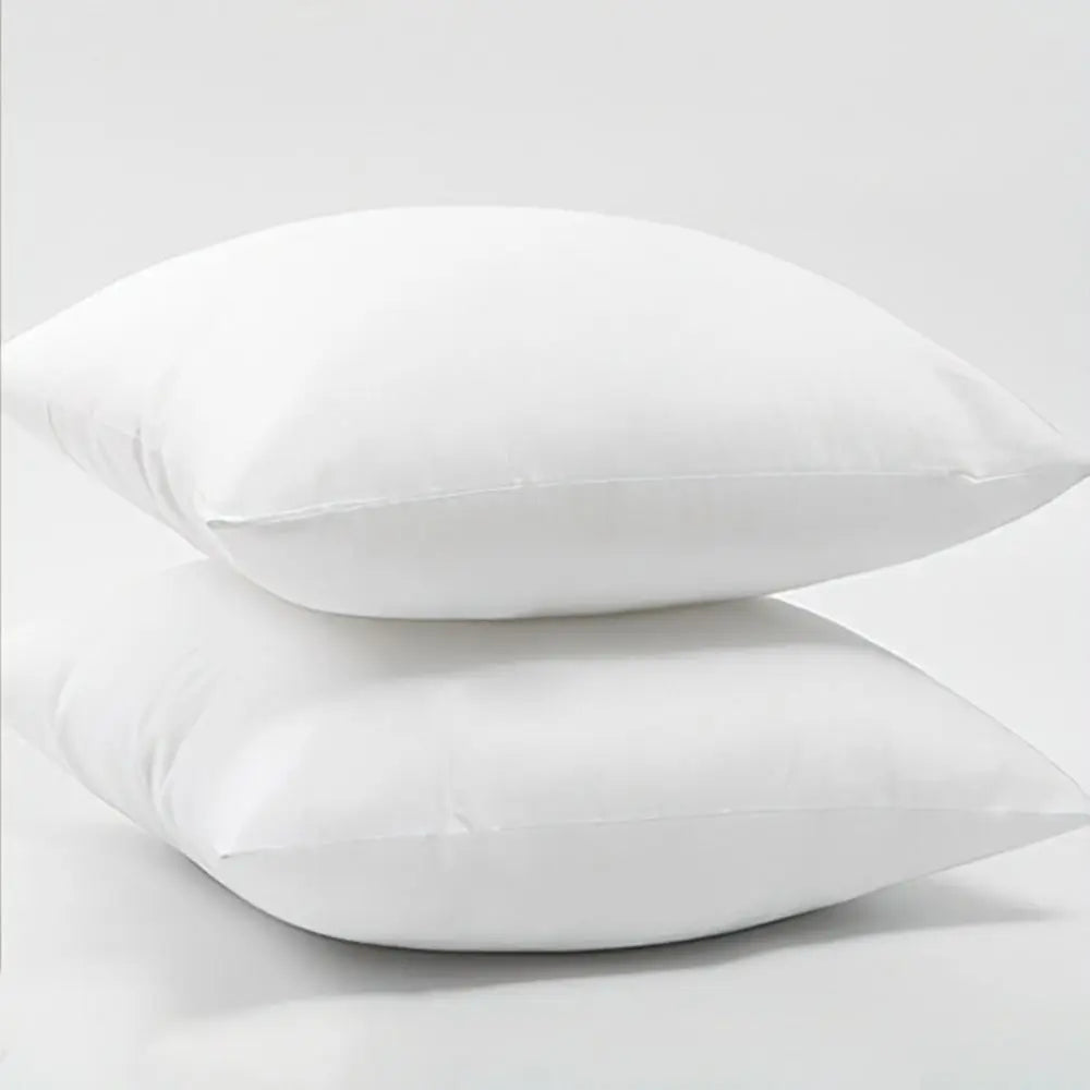 A pair of white cotton-filled decorative throw pillow inserts lying side by side.