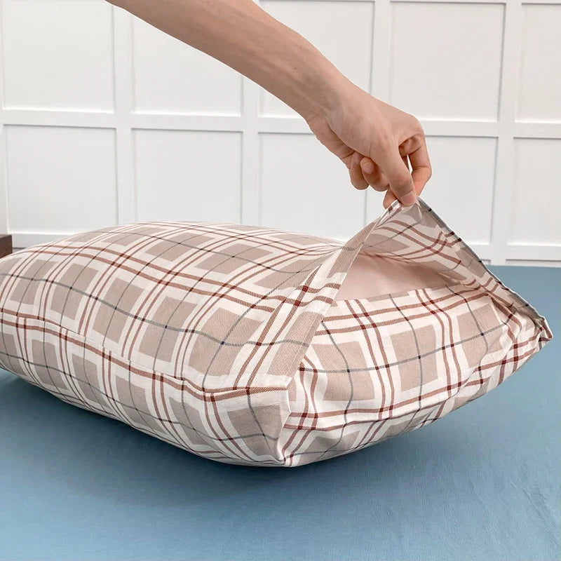A hand is adjusting a beige and brown plaid pillow cover on a light blue surface.