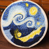 A cross stitch embroidery depicting a swirling night sky with yellow and blue stars and crescent moon.
