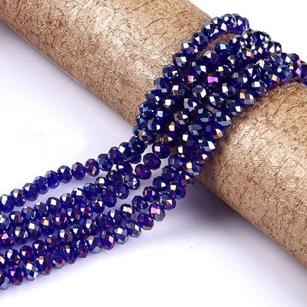 A strand of deep blue faceted rondelle glass beads is unwrapped and laid across a brown cylindrical object.