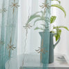 Light blue sheer curtains decorated with silver floral wave patterns and a potted green fern.
