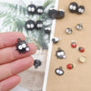 A hand holds a set of black and silver ladybug resin charms on a brown background.