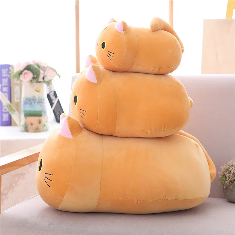 Three soft orange cat plush pillows stacked on a light surface.