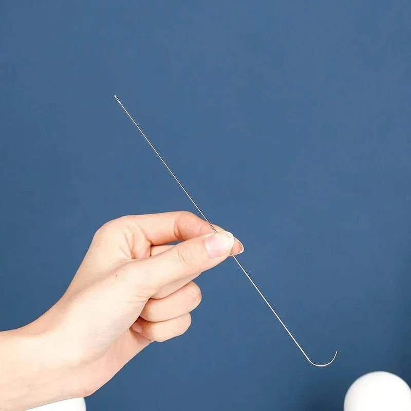 A hand is holding a thin stainless steel beading needle, demonstrating its use for crafting.