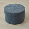 A round, gray jacquard ottoman footrest slipcover with a textured leaf pattern on a light wooden floor.