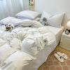 A white duvet cover set with pillows and a small stuffed animal on a bed.