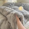 A hand is touching a fluffy gray rabbit fleece duvet cover on a bed.