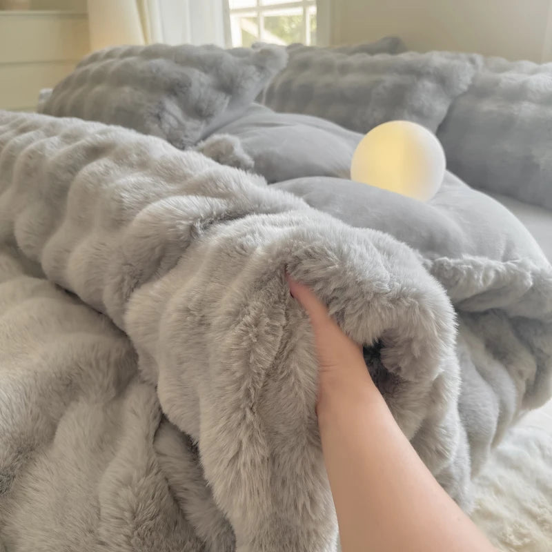 A hand is touching a fluffy gray rabbit fleece duvet cover on a bed.