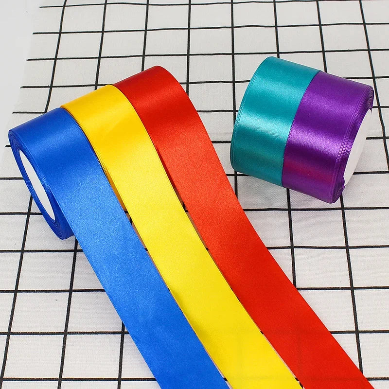 A collection of satin craft ribbons in blue, yellow, and red are laid diagonally on a white grid background.