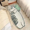 A cute cartoon cat plush mat with a green phone accessory lying on a light wooden floor.