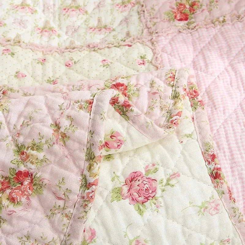 Close-up of a pink and white patchwork quilt fabric featuring floral patterns and quilted texture.