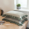 A set of two soft plaid washed cotton pillowcases with ruffled edges displayed on a light brown surface.