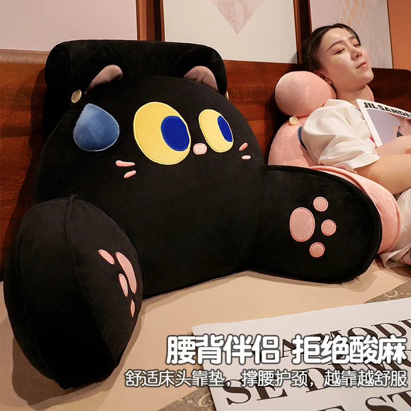 A black plush animal cushion with blue and yellow eyes is displayed next to a person.