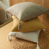 Three linen throw pillows in beige, mustard yellow, and natural linen fabric resting on a woven basket.