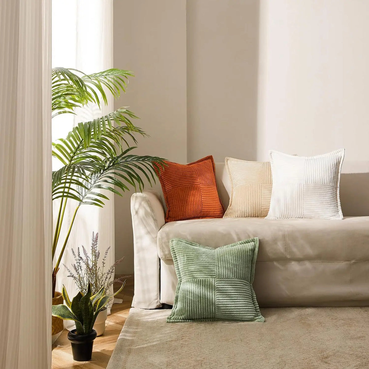 A close-up of a light beige sofa with various textured pillows including orange, cream, and green striped corduroy cushions.