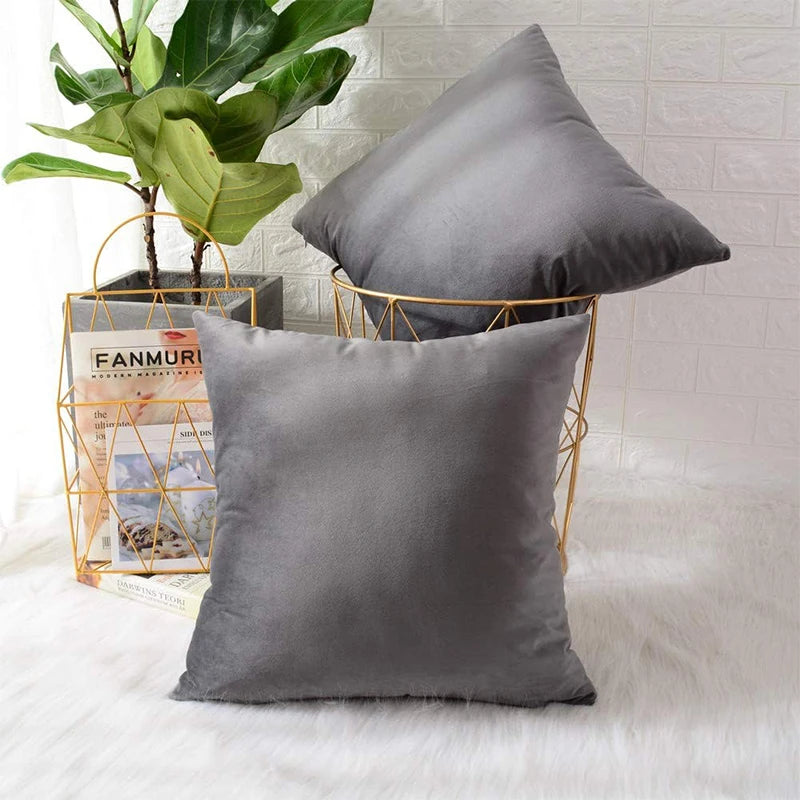 A gray velvet cushion cover resting on a gold wire stand next to a potted green plant.