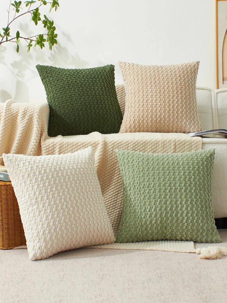 A collection of textured pillows in olive green, beige, and cream tones displayed on a light-colored sofa.
