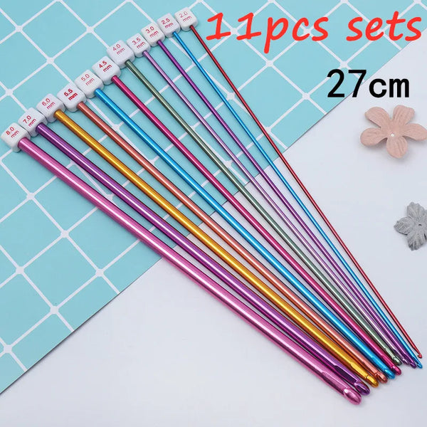 A set of 11 mixed-size Tunisian crochet hooks in various colors laid out on a blue grid.