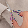 A hand is using vintage stainless steel sewing scissors to cut fabric on a light-colored garment.
