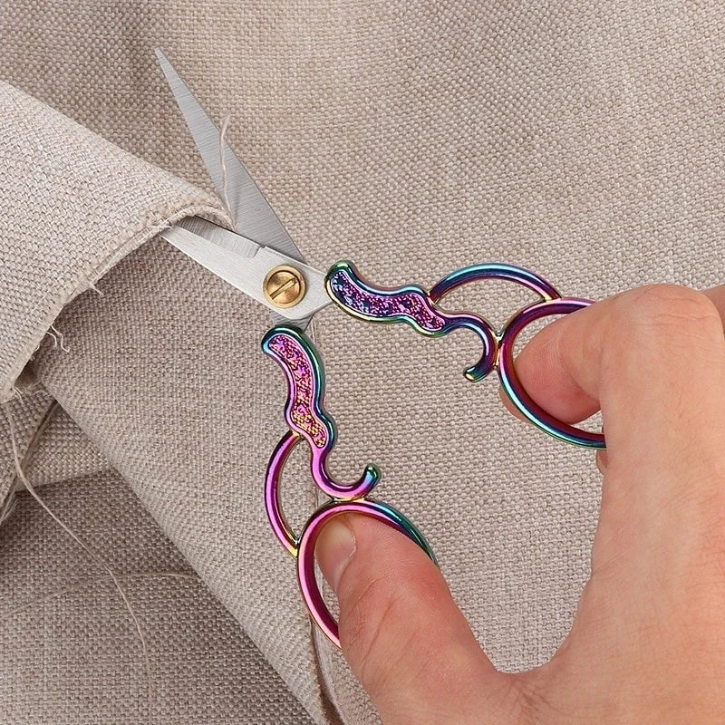 A hand is using vintage stainless steel sewing scissors to cut fabric on a light-colored garment.