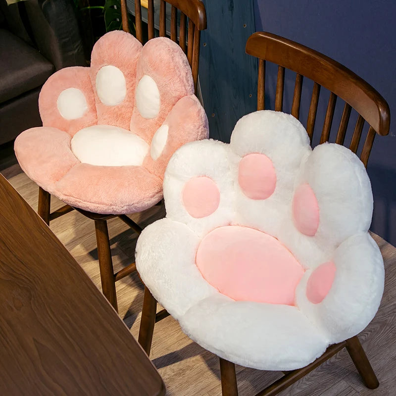 A pink and white plush bear paw cushion displayed on a wooden chair.