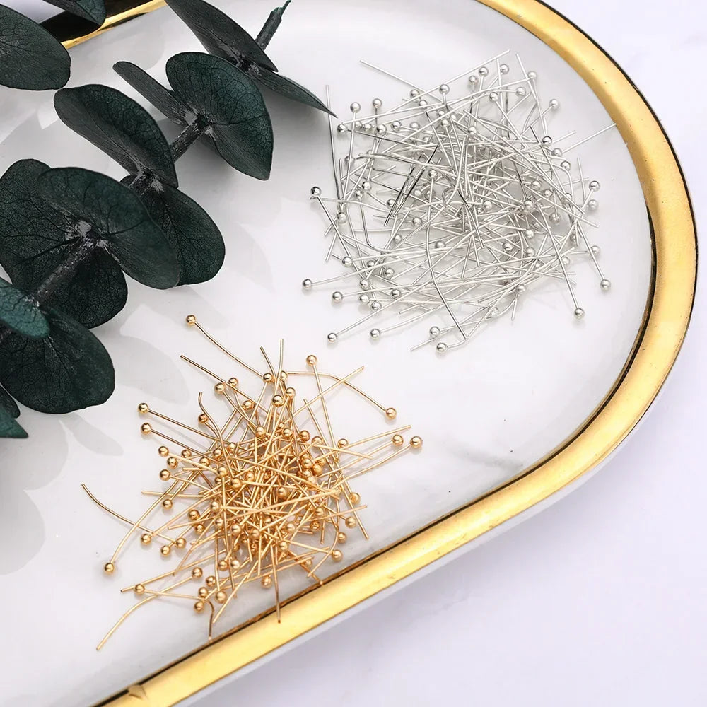 A close-up of stainless steel ball head pins for jewelry making, showing both silver and gold colored pins on a white surface