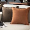 A close-up of a rust brown chenille throw pillow resting on a light beige sofa.