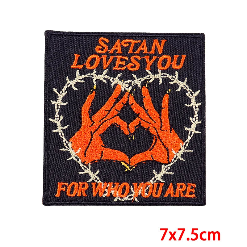 A black embroidery patch featuring the text Satan Loves You for who you are surrounded by a heart shape and thorny wreath.